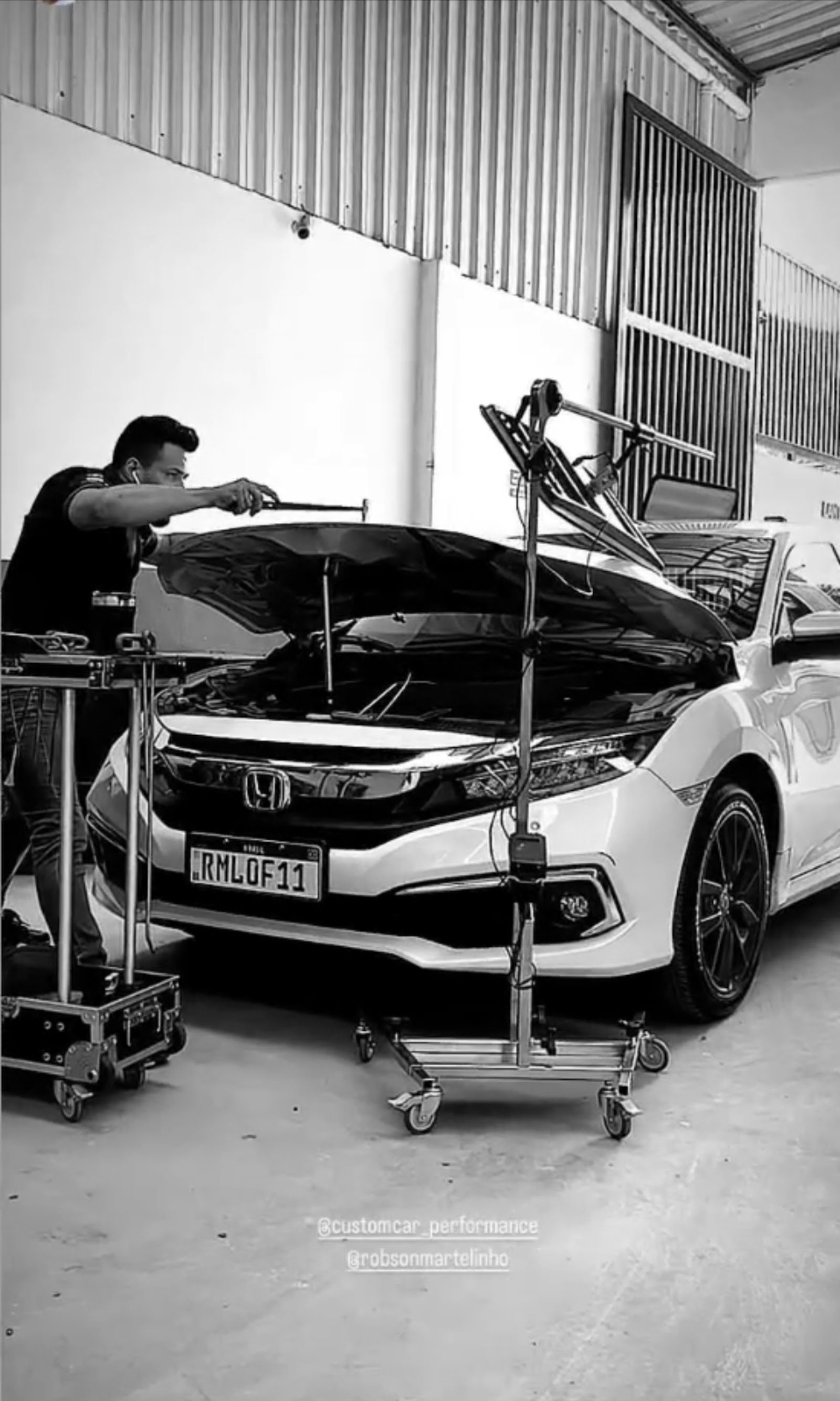 Reparo em andamento no capô de um Honda Civic branco, com haste de martelinho e placa refletora