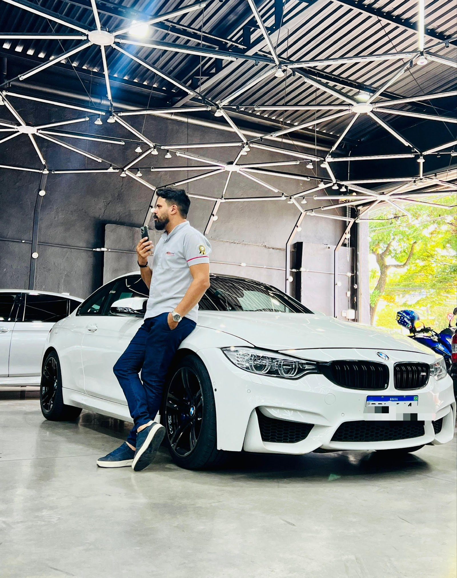 Homem de camisa da empresa encostado em um BMW branco dentro do galpão de atendimento