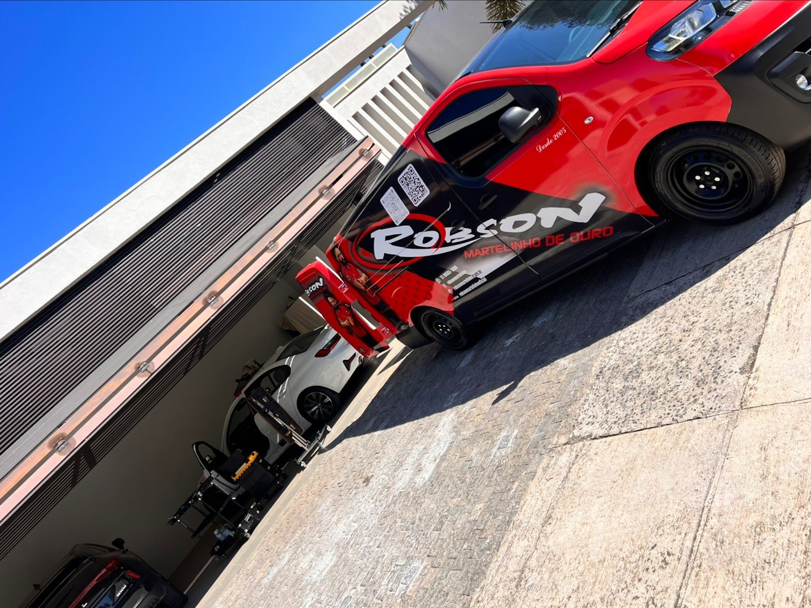 Van da empresa parada na entrada do galpão, com um carro em atendimento ao fundo