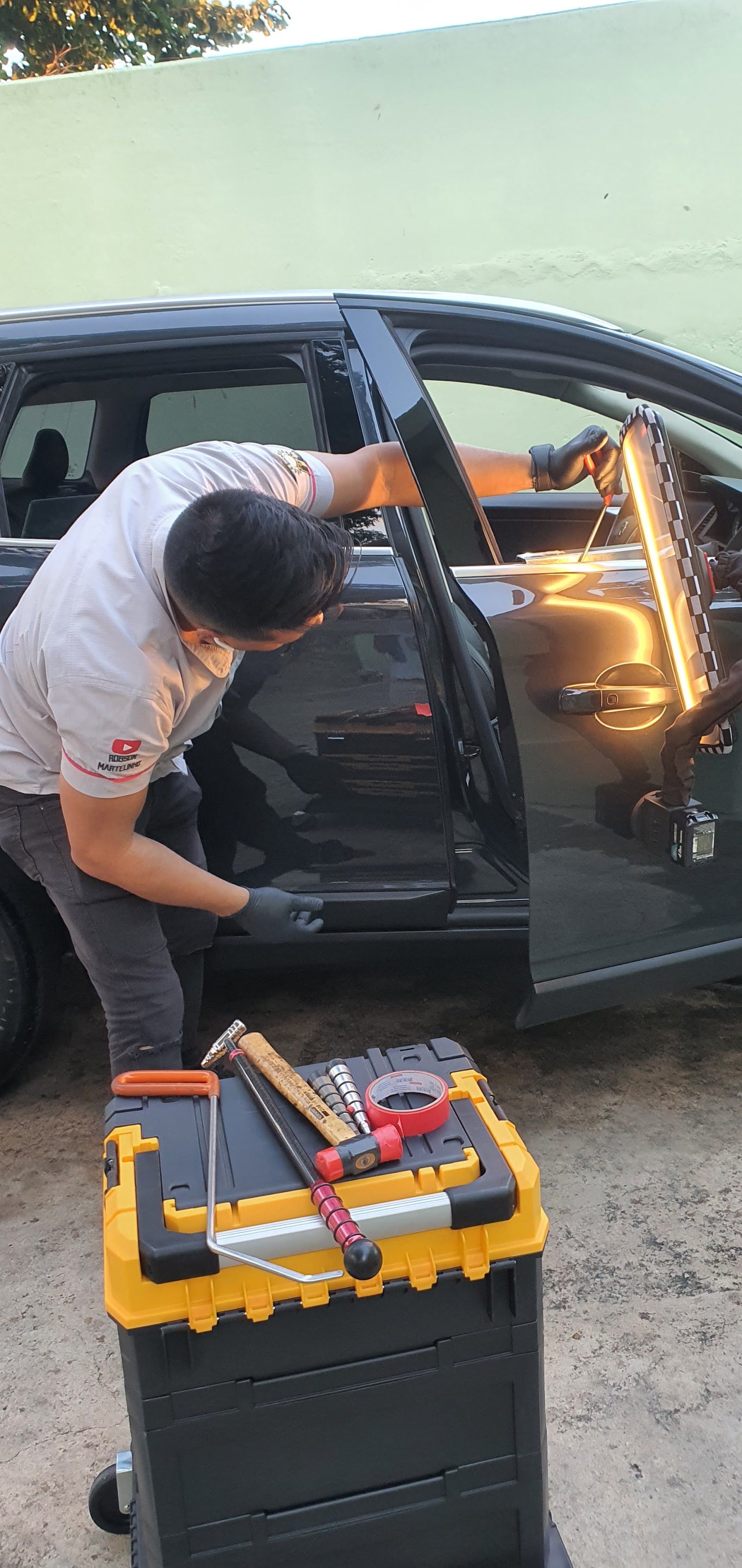 Robson trabalhando a porta de um carro preto com a placa de leitura e as hastes de martelinho